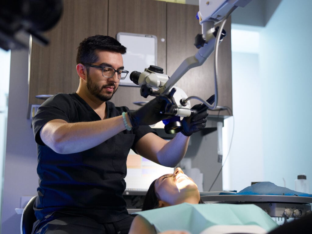 Dr. Rosenblatt using an advanced dental operating microscope to perform a precise examination on a patient who is reclining in a chair.