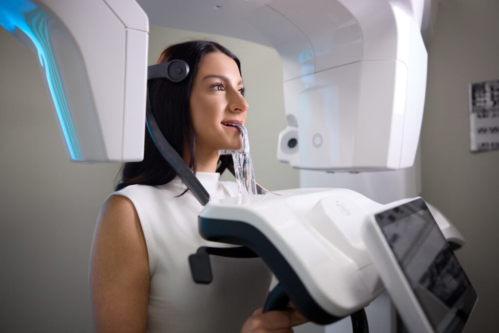 A female patient stands while positioned in a modern 3D dental imaging machine for a panoramic X-ray scan.
